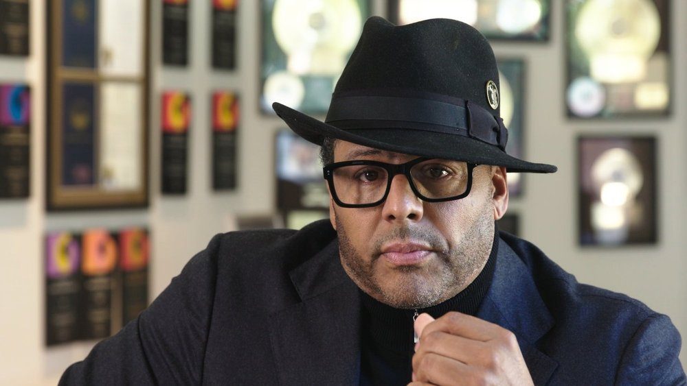 Al B. Sure! in a black hat in front of a wall of framed gold records