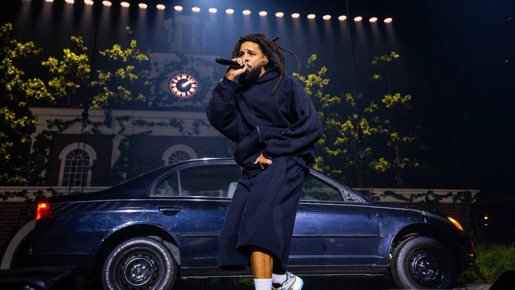 J. Cole rapping on a stage set with a vintage car