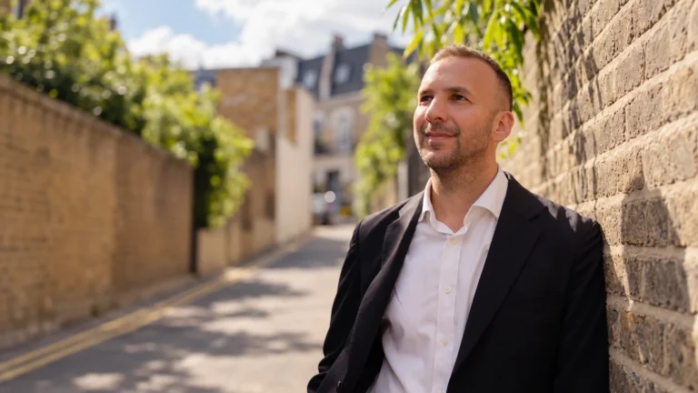 Zack Polanski, Green Party leader, leaning against a brick wall on a sunny London street